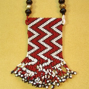 Puede incluir: Un collar de cuentas rojas y blancas con flecos y una peque&ntilde;a bolsa. La bolsa est&aacute; decorada con un patr&oacute;n de chevron.