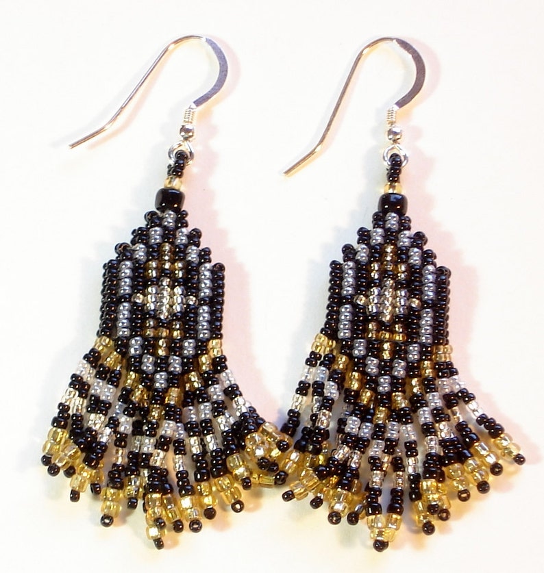 May include: Black, gold and silver beaded earrings with a fringe design. The earrings are made with small seed beads and have a silver hook fastening.