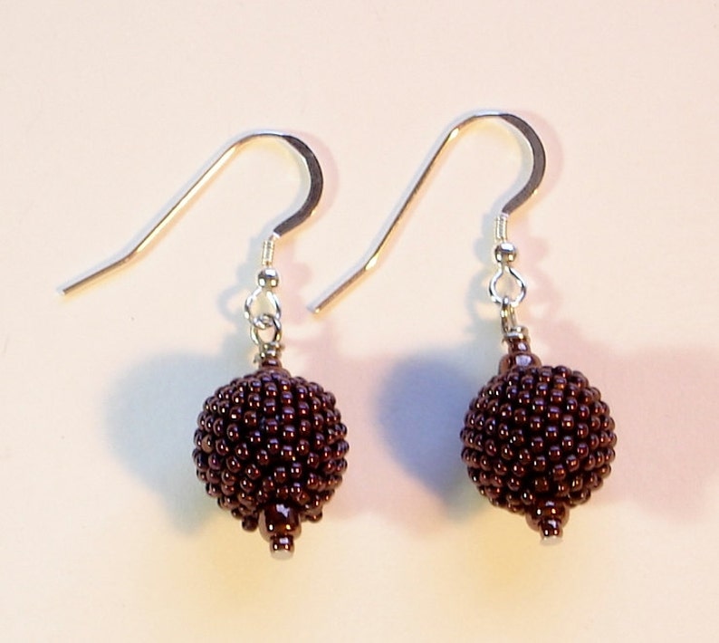 May include: A pair of brown beaded earrings with silver hooks. The beads are small and round, creating a textured, spherical shape.