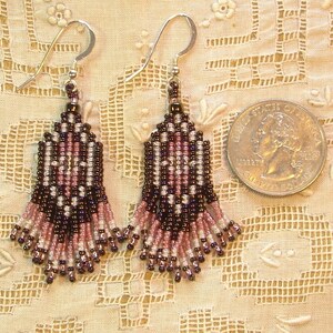 Peut inclure: Une paire de boucles d'oreilles perl&eacute;es avec des crochets en argent. Les boucles d'oreilles pr&eacute;sentent un motif g&eacute;om&eacute;trique dans les tons de noir, rose et blanc. Elles sont pr&eacute;sent&eacute;es &agrave; c&ocirc;t&eacute; d'une pi&egrave;ce de monnaie pour comparaison.