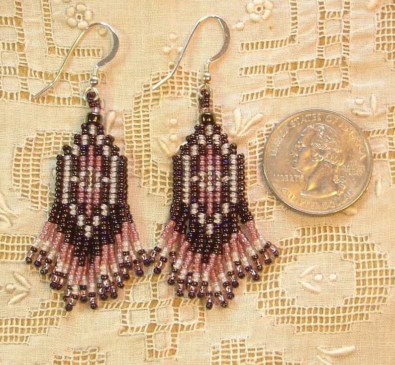 Peut inclure: Une paire de boucles d'oreilles perl&eacute;es avec des crochets en argent. Les boucles d'oreilles pr&eacute;sentent un motif g&eacute;om&eacute;trique dans les tons de noir, rose et blanc. Elles sont pr&eacute;sent&eacute;es &agrave; c&ocirc;t&eacute; d'une pi&egrave;ce de monnaie pour comparaison.