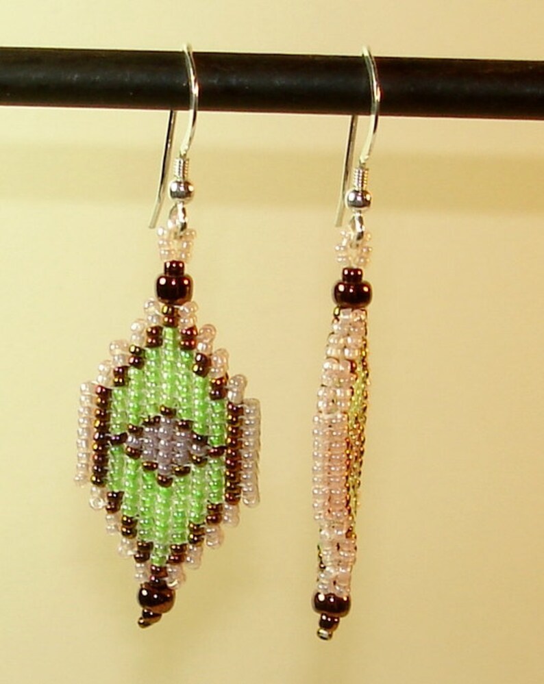 May include: A pair of green, brown, and white beaded earrings with silver hooks. The earrings are shaped like a diamond and have a geometric pattern.
