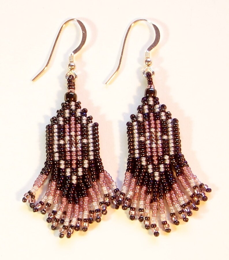 Peut inclure: Une paire de boucles d'oreilles perl&eacute;es avec des crochets argent&eacute;s. Les boucles d'oreilles pr&eacute;sentent un motif g&eacute;om&eacute;trique dans les tons noir, rose et blanc. La frange perl&eacute;e est en forme d'&eacute;ventail, cr&eacute;ant un design d&eacute;licat et &eacute;l&eacute;gant.