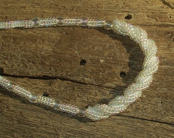 May include: A white beaded necklace with a twisted design. The necklace is made of small, iridescent beads that catch the light.