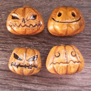May include: Four small, orange, carved pumpkin decorations with various facial expressions. Two have angry faces, one has a smiling face, and the last has a sad face. The pumpkins are on a wooden surface.