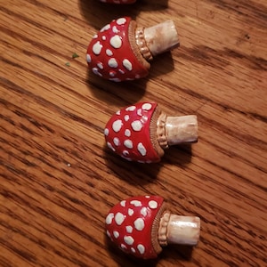 Könnte beinhalten: Fünf Keramik-Flaschenverschlüsse in Pilzform mit roten und weißen Details. Die Pilze haben einen braunen Stiel und einen roten Hut mit weißen Punkten.