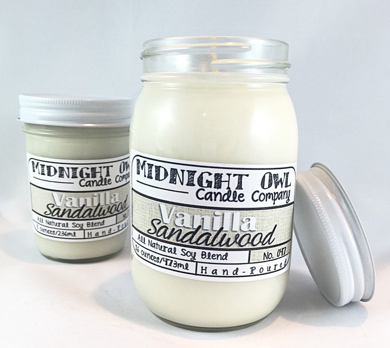 May include: Two glass jars with white lids containing vanilla sandalwood scented candles. The larger jar is labeled "Midnight Owl Candle Company Vanilla Sandalwood No. 047 14 ounces/473ml Hand-Poured". The smaller jar is labeled "Midnight Owl Candle Company Vanilla Sandalwood 7 ounces/236ml Hand-Poured".