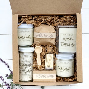 May include: A brown cardboard box filled with bath and body products. The box contains a bath bomb, a candle, a sugar scrub, a wax tart, a bar of soap, and a small jar of matches. The products are all labeled with the words "midnight owl" and have different scents, such as "calm", "relax", and "sugar scrub".