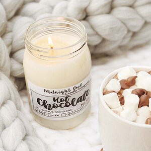 K&ouml;nnte beinhalten: Eine wei&szlig;e Kerze in einem Glasgef&auml;&szlig; mit einem Etikett, auf dem "Midnight Owl Candle Company Hot Chocolate No. 102 All Natural Soy Blend 8 Ounces/473 ML Hand Poured Candle" steht.