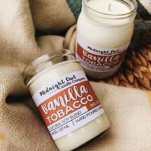 May include: Two glass candle jars with white wax and labels. The labels are brown with white text that reads "Midnight Owl Candle Company" and "Vanilla Tobacco". The smaller jar has the text "No. 031" and "All Natural Soy Blend 8 ounces/237 ml Hand Poured Candle".