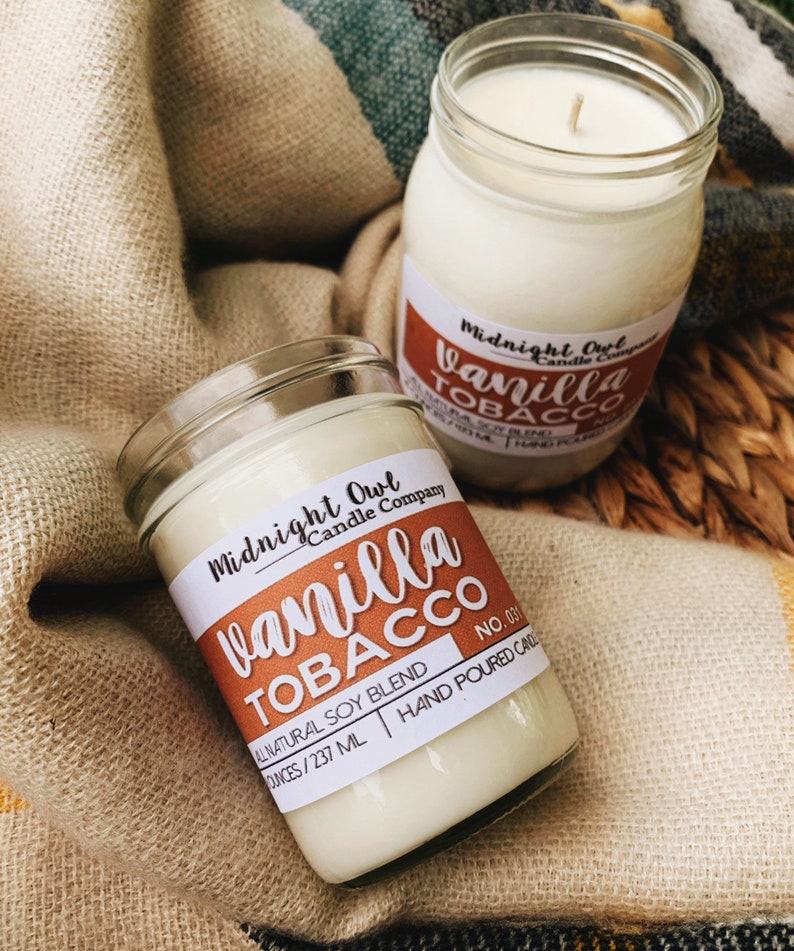 May include: Two glass candle jars with white wax and labels. The labels are brown with white text that reads "Midnight Owl Candle Company" and "Vanilla Tobacco". The smaller jar has the text "No. 031" and "All Natural Soy Blend 8 ounces/237 ml Hand Poured Candle".