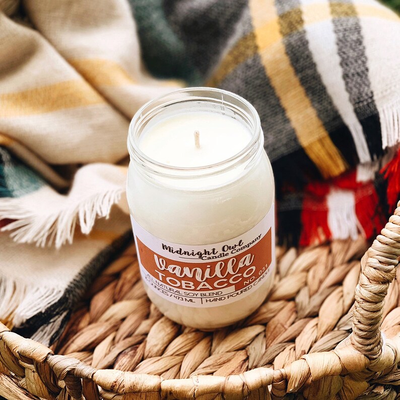 May include: A glass jar candle with a white label that reads "Midnight Owl Candle Company" and "Vanilla Tobacco No. 031". The label also says "Natural Soy Blend" and "8 oz / 237 ml - Hand Poured Candle". The candle is sitting on a woven basket.