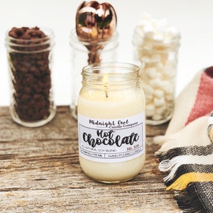 K&ouml;nnte beinhalten: Eine brennende Kerze in einem durchsichtigen Glasgef&auml;&szlig; mit einem wei&szlig;en Etikett, auf dem "Midnight Owl Candle Company Hot Chocolate No. 109 All Natural Soy Blend 8 Ounces / 213 ML Hand Poured Candle" steht.