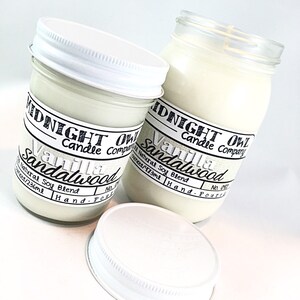 May include: Two glass jars with white lids filled with white candle wax. The jars have black labels with the text "Midnight Owl Candle Company" and "Vanilla Sandalwood" with the text "Natural Soy Blend" and the size in ounces and milliliters.