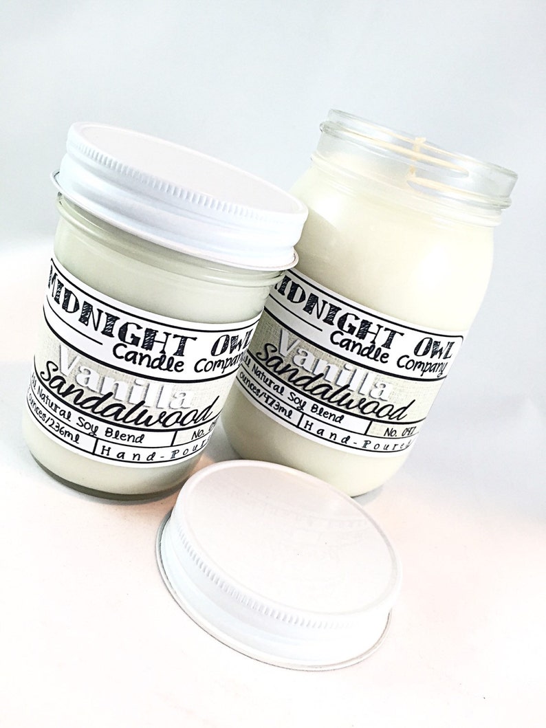 May include: Two glass jars with white lids filled with white candle wax. The jars have black labels with the text "Midnight Owl Candle Company" and "Vanilla Sandalwood" with the text "Natural Soy Blend" and the size in ounces and milliliters.