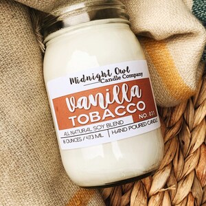 May include: A glass jar candle with a white label that reads "Midnight Owl Candle Company" and "vanilla TOBACCO NO. 031". The label also says "All Natural Soy Blend 16 ounces / 473 ml Hand Poured Candle".