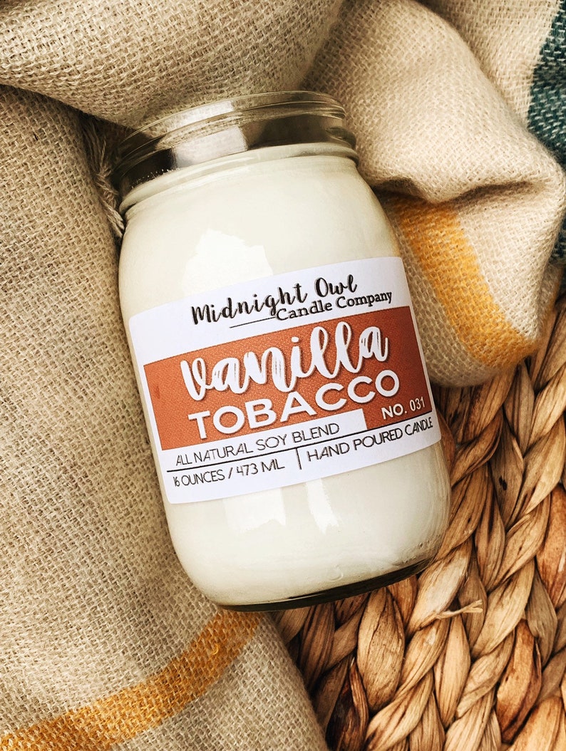 May include: A glass jar candle with a white label that reads "Midnight Owl Candle Company" and "vanilla TOBACCO NO. 031". The label also says "All Natural Soy Blend 16 ounces / 473 ml Hand Poured Candle".