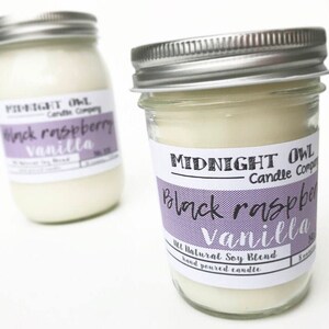 May include: Two glass jars with silver lids filled with a white candle. The labels on the jars read "Midnight Owl Candle Company" and "Black Raspberry Vanilla". The jars are on a white surface.
