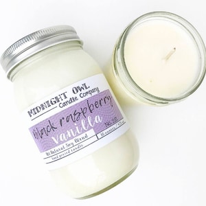 May include: Two glass jars with lids, one filled with a white candle and the other with a white candle with a label that reads "MIDNIGHT OWL Candle Company Black Raspberry Vanilla No. 281 16 ounces / 473 ml"