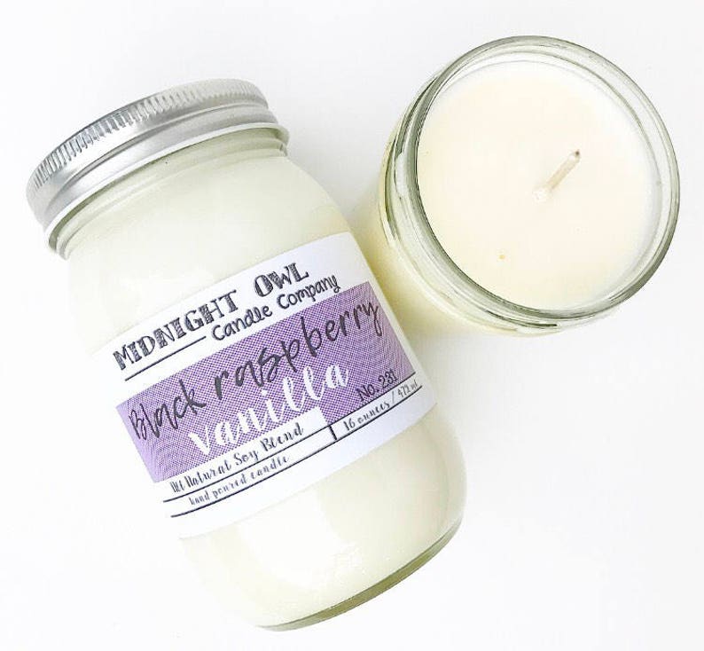 May include: Two glass jars with lids, one filled with a white candle and the other with a white candle with a label that reads "MIDNIGHT OWL Candle Company Black Raspberry Vanilla No. 281 16 ounces / 473 ml"