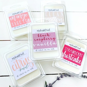 Puede incluir: Cinco fundidos de cera en recipientes de pl&aacute;stico transparente con etiquetas. Las etiquetas son de color rosa, rojo y blanco con texto que dice "Midnight Owl Candle Company" y varios aromas, que incluyen "Mango Sage Tea", "Clean Cotton", "Black Raspberry Vanilla", "Citrus & Basil" y "Strawberry Shortcake".
