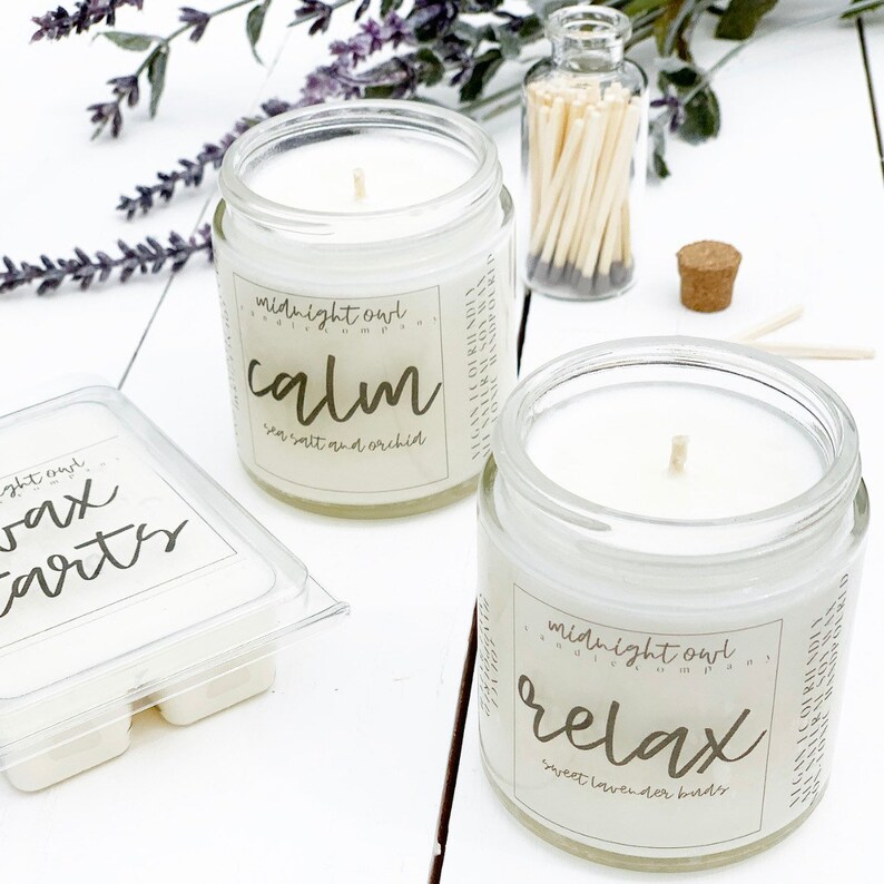 May include: Two glass candle jars with white wax and wooden wicks. The jars have labels that read "midnight owl candles" and the scents "calm sea salt and orchid" and "relax sweet lavender buds".