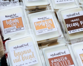 May include: A collection of nine wax melts in clear plastic containers with labels. The labels are white with black text and feature different scents, including Caramel Macchiato, Oatmeal Milk + Honey, Fresh Baked Cinnamon Rolls, Autumn Leaves, Pumpkin Roll, Caramel Pecan Pie, Banana Nut Bread, and Vanilla Tobacco. The wax melts are all natural soy blend and hand-poured.