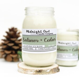 K&ouml;nnte beinhalten: Eine Kerze in einem Glasgef&auml;&szlig; mit einem wei&szlig;en Etikett, auf dem "Midnight Owl Candle Company Balsam + Cedar" und "All Natural Soy Blend 8 ounces/473ml Hand Poured Candle No. 041" steht.