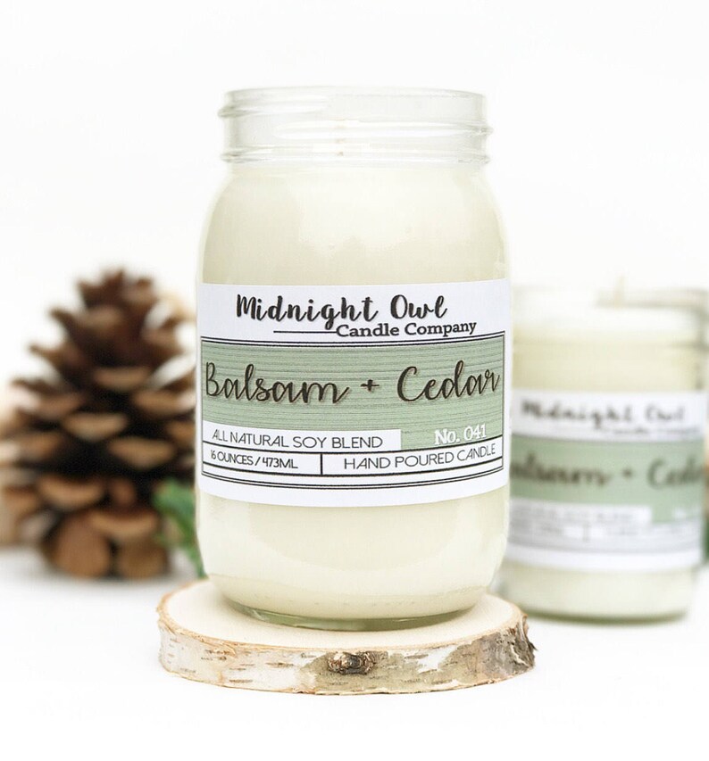 K&ouml;nnte beinhalten: Eine Kerze in einem Glasgef&auml;&szlig; mit einem wei&szlig;en Etikett, auf dem "Midnight Owl Candle Company Balsam + Cedar" und "All Natural Soy Blend 8 ounces/473ml Hand Poured Candle No. 041" steht.