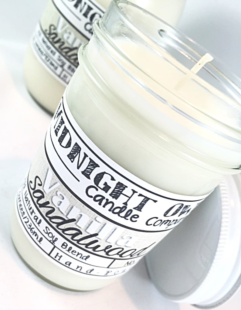 May include: A glass jar candle with a white label that reads "Midnight Candle Company Vanilla & Sandalwood". The candle is hand-poured with a natural soy blend and is 4 oz (123 ml).