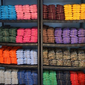 May include: A shelf unit filled with stacks of colorful bean bags. The bean bags are arranged in rows on the shelves, with each row featuring a different color. The colors include blue, pink, brown, yellow, purple, orange, light blue, dark blue, gray, green, and red.