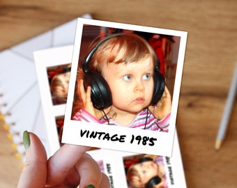 May include: A square instant film print featuring a child wearing black over-ear headphones, with the text VINTAGE 1985 printed in black ink at the bottom. The print is held up, showing a white border and a glossy finish on the photograph.