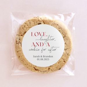 Pode incluir: Um adesivo redondo branco com o texto "LOVE, laughter, AND A cookie for after" em letras pretas e vermelhas. O adesivo está em um biscoito marrom em um saco de plástico transparente.