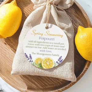 Può includere: Un sacco di iuta legato con spago, con un'etichetta che recita "Spring Simmering Potpourri". L'etichetta include istruzioni e un'illustrazione di limone e lavanda. Due limoni freschi sono su un vassoio di legno.
