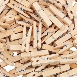May include: A pile of natural wooden clothes pegs with metal springs. The clothes pegs are all the same size and shape, and they are arranged in a random pattern.