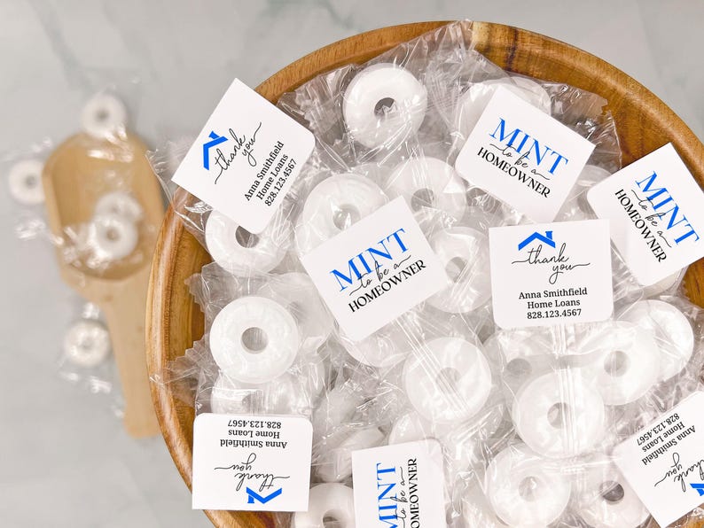 May include: A wooden bowl filled with individually wrapped white mint candies. Each candy wrapper has the text "MINT to be a HOMEOWNER" in blue and white, along with a thank you message and contact information.