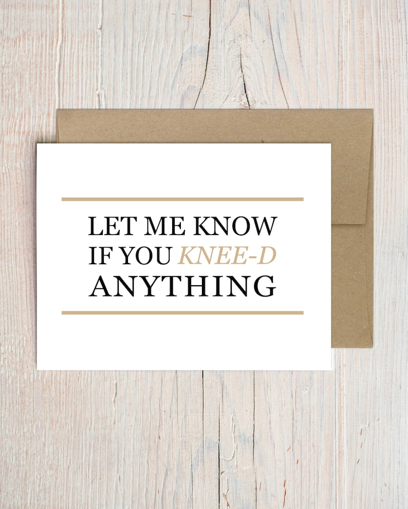 May include: A white greeting card with the text "LET ME KNOW IF YOU KNEE-D ANYTHING" in black and tan font, with tan lines above and below the text. The card is inside a brown envelope, set against a light wood grain background.