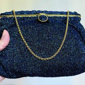 May include: A vintage beaded handbag in a deep navy blue color with a gold chain strap. The bag has a structured shape with a clasp closure and is covered in small, shimmering beads.