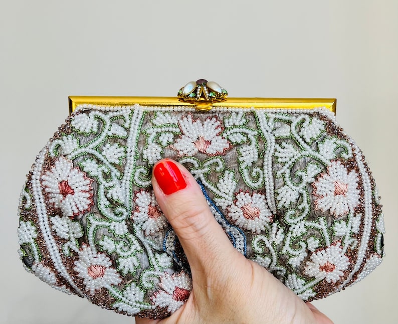 May include: A white beaded clutch purse with a floral design and a gold metal frame. The purse is decorated with small white beads and pink and green accents.