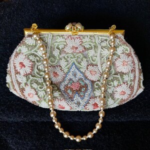 May include: A white beaded evening bag with a floral design and a pearl chain strap. The bag has a gold clasp and a decorative floral embellishment.