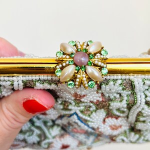 May include: A vintage beaded evening bag with a gold clasp and a floral-shaped closure with green and white stones and a pink center stone.