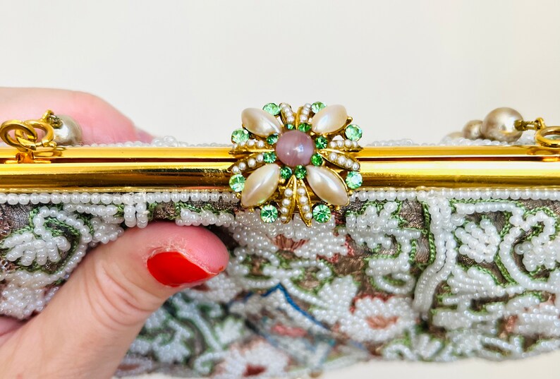 May include: A vintage beaded evening bag with a gold clasp and a floral-shaped closure with green and white stones and a pink center stone.