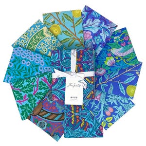 May include: A set of eight fabric squares featuring a variety of floral and botanical patterns in shades of blue, green, and purple. The fabric squares are arranged in a circle and have a white label with the text "Free Spirit" in the center.