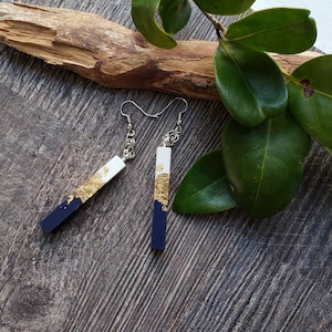 May include: A pair of dangle earrings with a black and white rectangular design. The earrings are accented with gold leaf and have silver hooks.