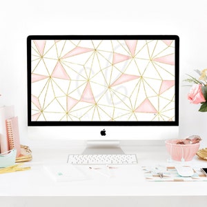 May include: A white desktop computer with a pink and gold geometric pattern wallpaper displayed on the screen. The computer is on a white desk with a keyboard, a pink bowl, a vase of pink flowers, and other office supplies.