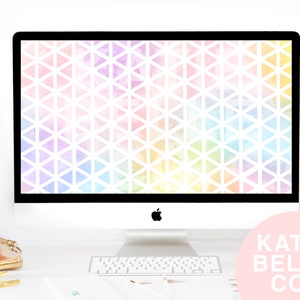May include: A white desktop computer with a colorful geometric pattern wallpaper on the screen. The computer is on a white desk with a keyboard and a pink logo that says "KATIE BELLE CO."