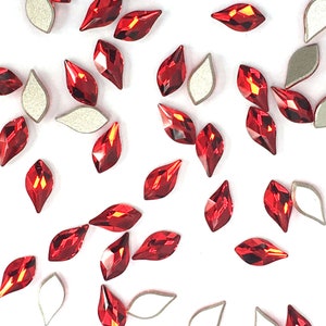 Pode incluir: Uma dispersão de strass de cristal vermelho em forma de lágrima. Os strass estão dispersos sobre um fundo branco.