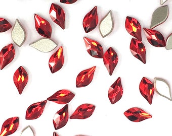 May include: A scattering of red crystal rhinestones in a teardrop shape. The rhinestones are scattered on a white background.