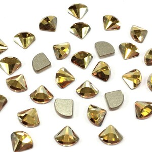 Può includere: Una collezione di strass sfaccettati color ambra in varie forme, tra cui triangoli e semicerchi. Gli strass sono sparsi su una superficie bianca, evidenziando le loro qualità riflettenti, adatti per lavori artigianali o gioielli.