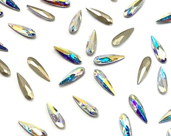 May include: A collection of iridescent teardrop-shaped rhinestones, scattered on a white background.